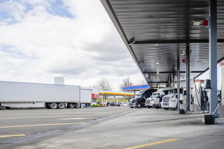 Long haul big rigs semi trucks with semi trailers standing on the truck stop fuel station refueling tanks for freights continuation each according to its own schedule of movement and delivery